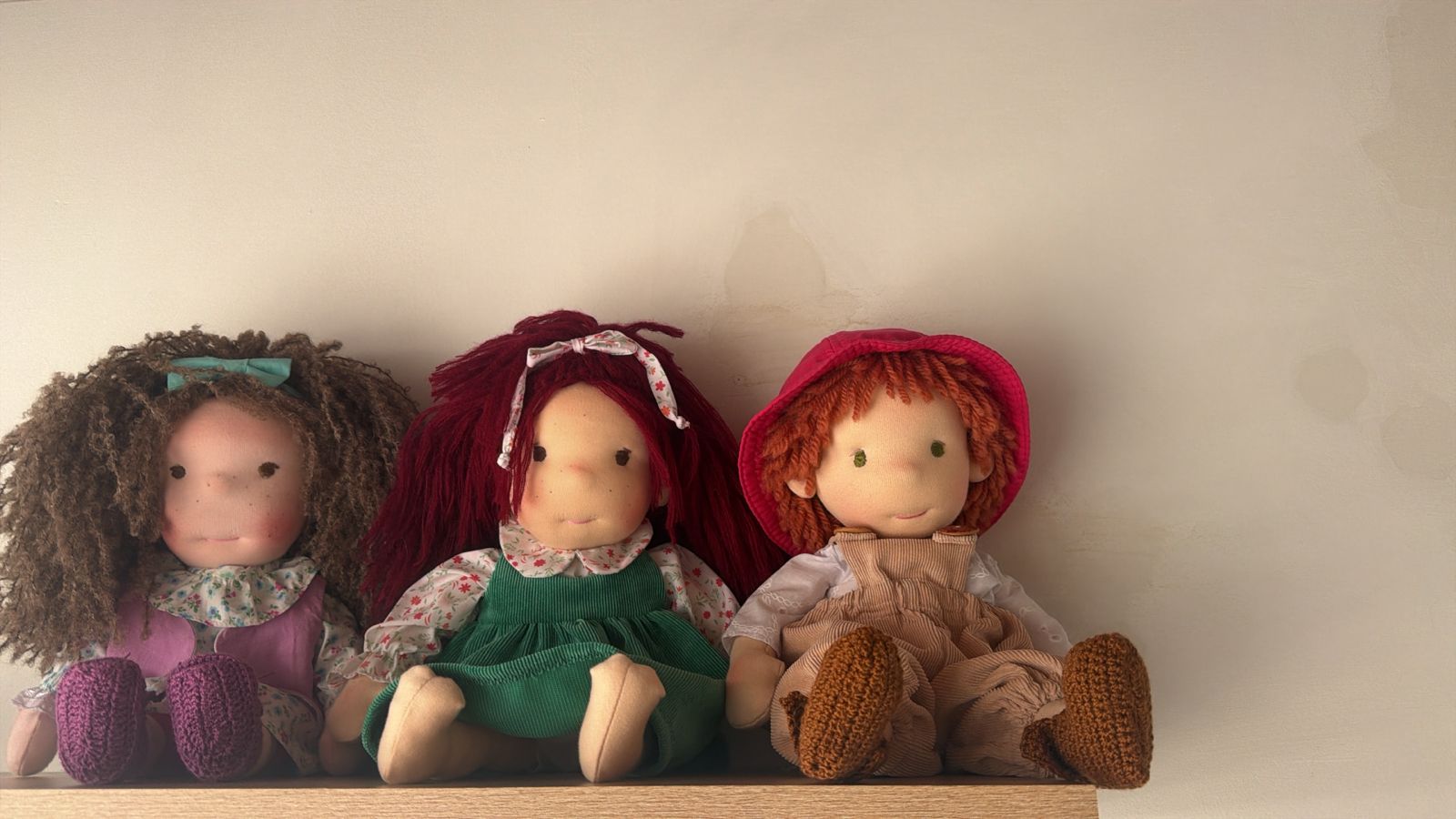 Tres muñecas sentadas en una repisa, cada una con un pelo y una ropa distintos.